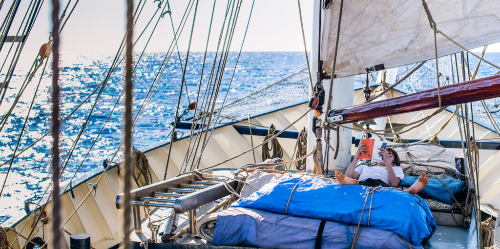 Summer tuition: student life at sea. S teenage boy reading aboard the Thalassa boat in the ocean as part of the School at Sea programme